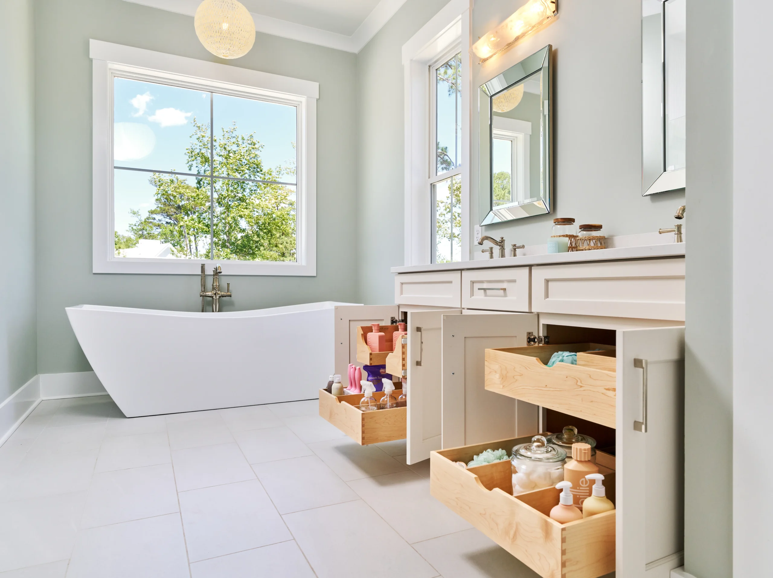A modern bathroom with a freestanding white bathtub, a double vanity, and open cabinet drawers revealing organized toiletries A modern bathroom with a freestanding white bathtub, a double vanity, and open cabinet drawers revealing organized toiletries