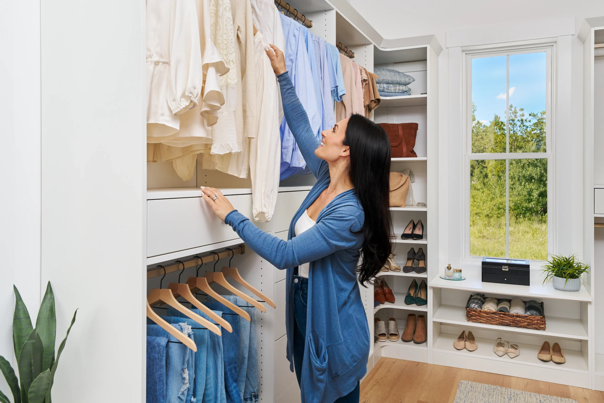 A woman in a white closet with organized clothes on shelves and hanging rods, reaching for a shirt A woman in a white closet with organized clothes on shelves and hanging rods, reaching for a shirt