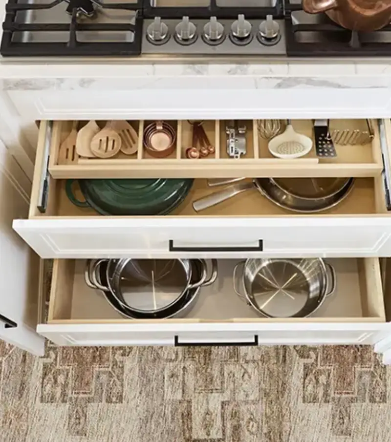 An overhead view of three open kitchen drawers, revealing a variety of pots, pans, and utensils in an organized layout